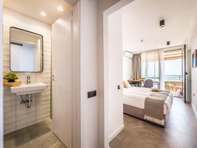 Lichte hotelkamer met groot bed en aangrenzende badkamer met wastafel en spiegel.