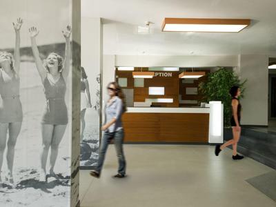 Hotelhal met een receptie, twee mensen en een grote muurschildering van zwemmers.