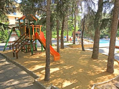 Spielplatz mit Rutsche und Klettergerüst neben einem Swimmingpool in einem bewaldeten Bereich.