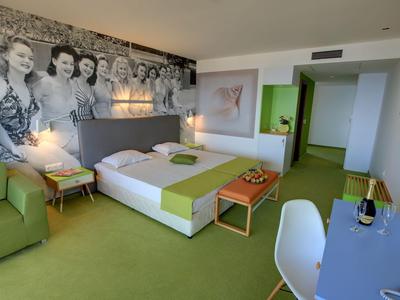 Modernes Hotelzimmer mit grünem Teppich, Doppelbett, Sitzbereich und Schreibtisch.