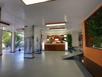 Moderne hotel lobby met receptiebalie, zuilen en plantenarrangementen.