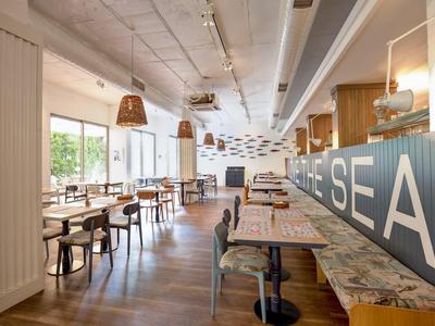 Modernes, helles Café mit Holztischen, Stühlen, großen Fenstern und maritimer Dekoration.