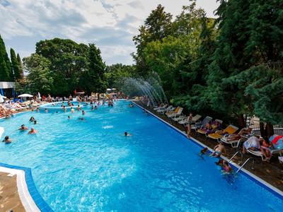 Belebtes Schwimmbecken mit Gästen, umgeben von Liegestühlen und Bäumen.