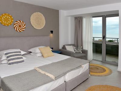 Moderne hotelkamer met tweepersoonsbed, bank en balkon met uitzicht op zee.