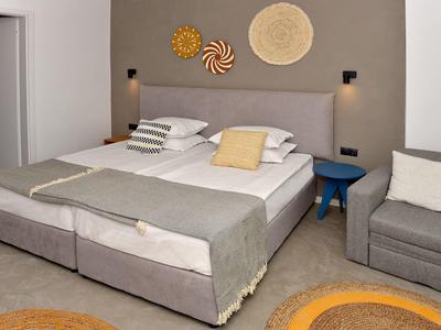 Modern hotelkamer met tweepersoonsbed, grijze bank en blauwe nachtkastlamp.