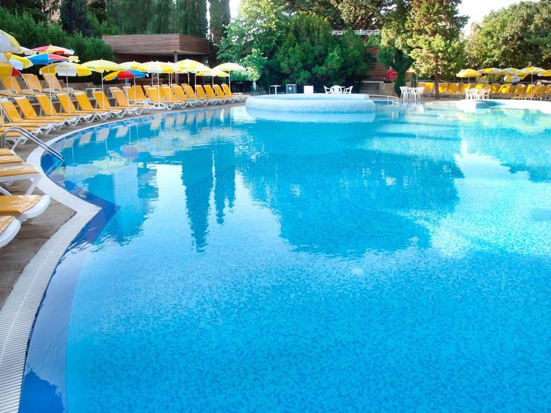 Groot blauw zwembad met veel gele ligstoelen bij zonnig weer.
