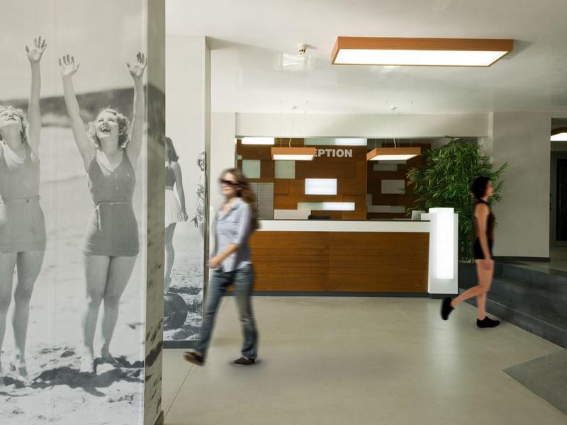 Hotelhal met een receptie, twee mensen en een grote muurschildering van zwemmers.