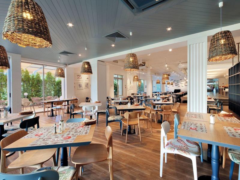 Modern restaurant met houten vloeren, grote ramen en rotan lampen.