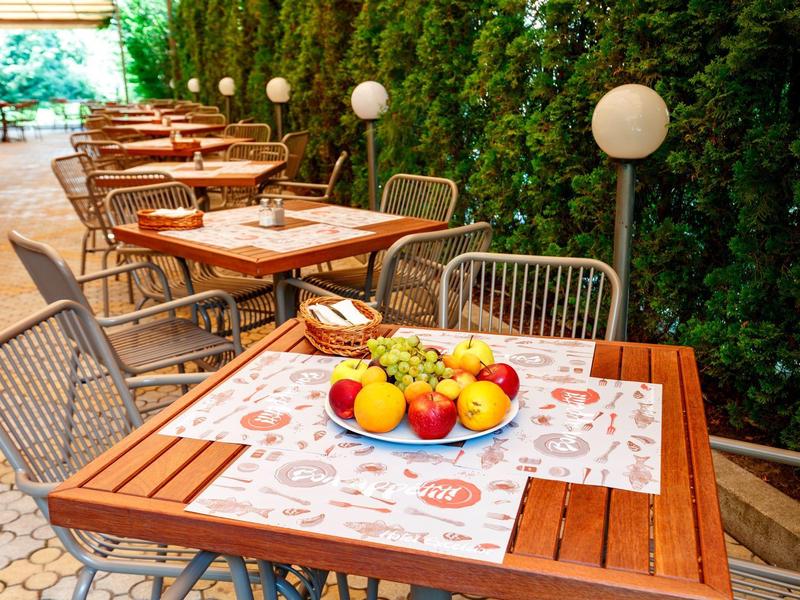 Gezellig buitenterras met houten tafels en stoelen, versierd met fruit en een groene haag.