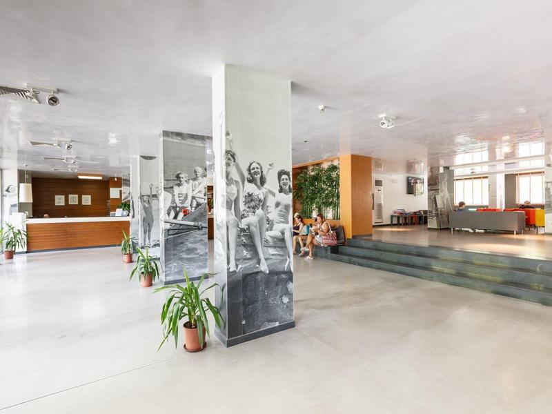 Ruime hotellobby met witte vloer, zitgedeeltes en planten.