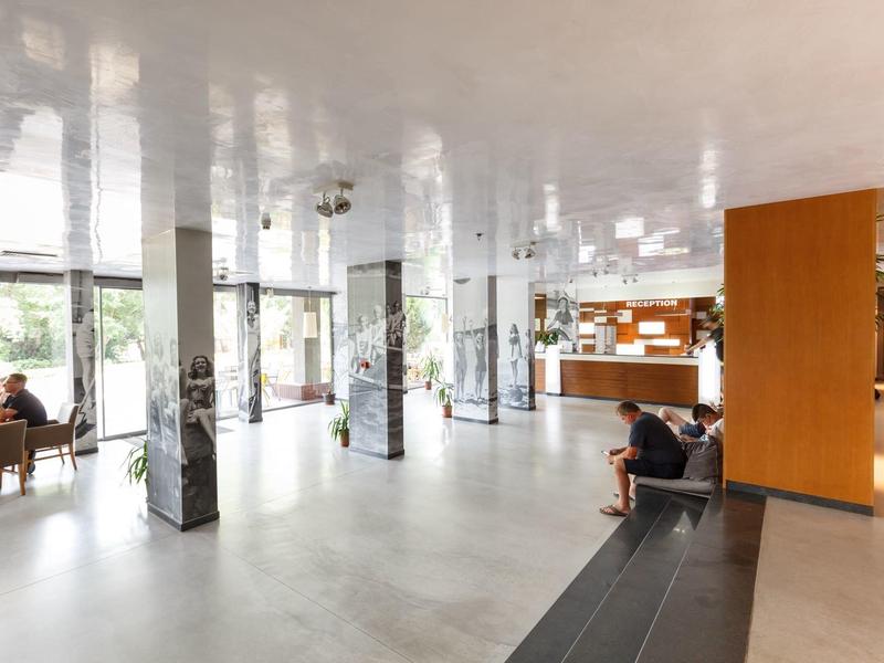 Lichte hotellobby met zitplaatsen, receptie en grote ramen met uitzicht naar buiten.