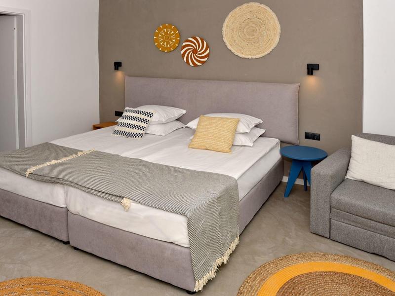 Modern ingerichte hotelkamer met tweepersoonsbed, grijze accenten en gezellige zithoek.