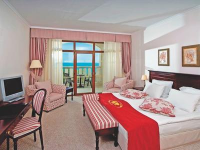 Helles Hotelzimmer mit großem Bett, Schreibtisch, Sesseln und Balkon mit Meeresblick.