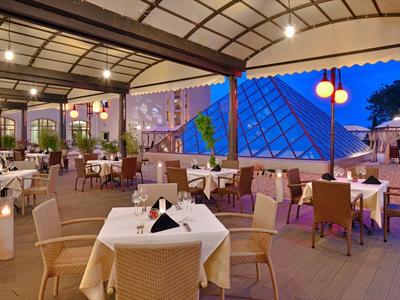 Abendliche Terrasse eines Hotels mit gedeckten Tischen und Blick auf modernes Glaspyramidengebäude.