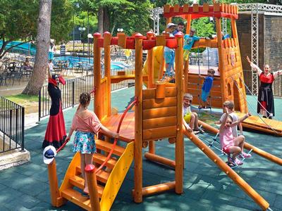 Kinder spielen auf einem hölzernen Klettergerüst im Hotelspielplatz an einem sonnigen Tag.