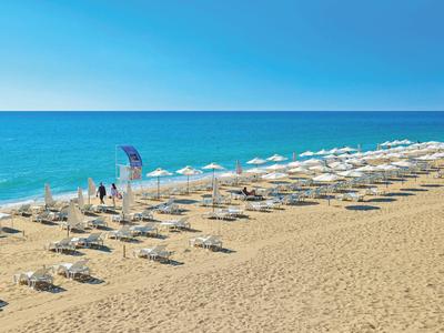 Strand mit Sonnenliegen und weißen Sonnenschirmen am Meer unter klarem Himmel.