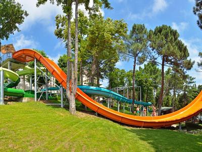 Wasserrutsche in einem grünen Park mit Bäumen und blauem Himmel im Hintergrund.