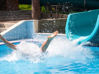 Eine Person rutscht mit Armen in die Luft aus einer blauen Wasserrutsche in einen Pool.