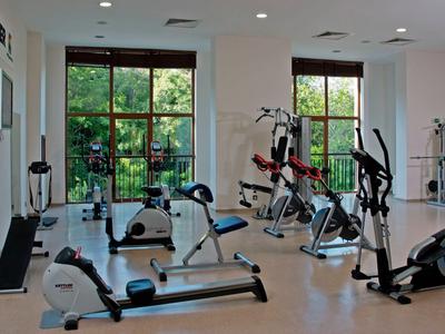 Heller Fitnessraum mit Fahrradergometern und Rudergeräten vor großen Fenstern mit Blick ins Grüne.