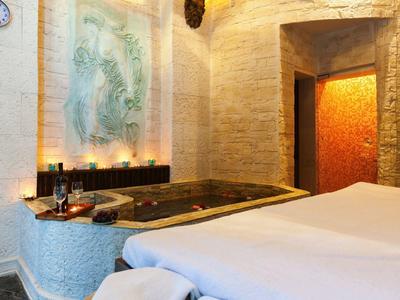 Gemütlicher Wellnessbereich mit großer Badewanne, Massagetisch und warmem Licht in beigen Tönen.