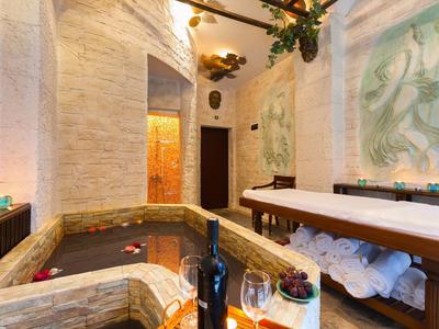 Gemütlicher Wellnessraum mit Kerzen, Weinglas, Whirlpool und Massagebank.