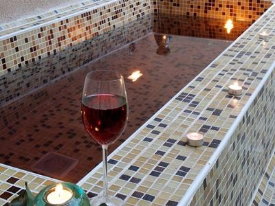 Ein rechteckiges Mosaikbad mit rotem Wasser, Kerze und Glas Rotwein auf der Kante.