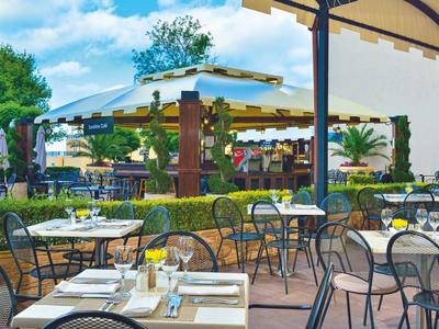 Terrasse eines Cafés mit gedeckten Tischen und Stühlen unter einem Sonnendach.