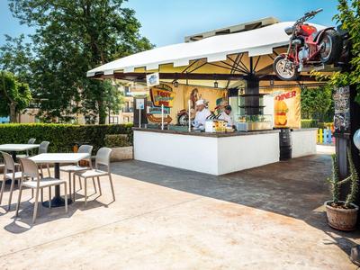 Moderner Außenbarbereich mit Stühlen, Tischen und einem schattigen Sonnenschirm, Motorrad-Dekoration oben.