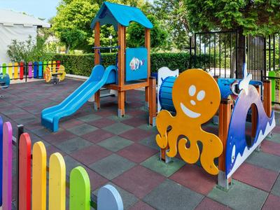 Bunter Spielplatz mit Rutsche und Oktopus-Spielgeräten, umgeben von einem farbigen Zaun.