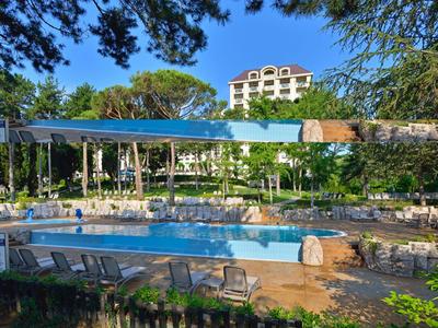 Poolbereich eines Hotels mit Sonnenliegen und umgeben von Bäumen und einem mehrstöckigen Gebäude im Hintergrund