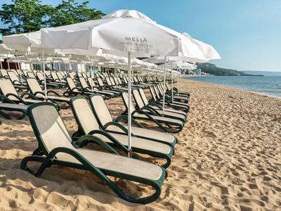 Strand mit Reihen von Liegestühlen und weißen Sonnenschirmen nahe dem Meer