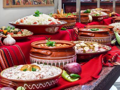 Verschiedene traditionelle Gerichte in braunen Tonvasen auf einem mit rotem Stoff bedeckten Tisch.