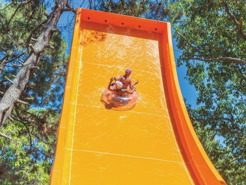 Menschen rutschen auf einer orangefarbenen Wasserrutsche im Freien bei sonnigem Wetter