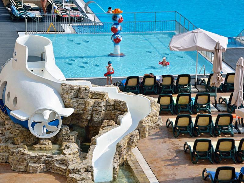 Wasserpark mit Rutsche, Schwimmbecken und Liegestühlen neben dem Meer.