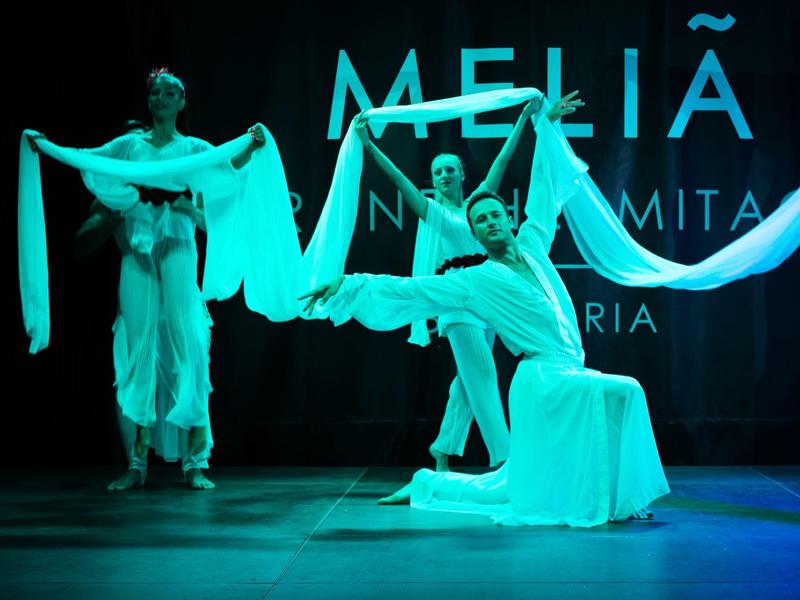 Drei Frauen in weißen Gewändern tanzen auf einer Bühne mit blauer Beleuchtung.