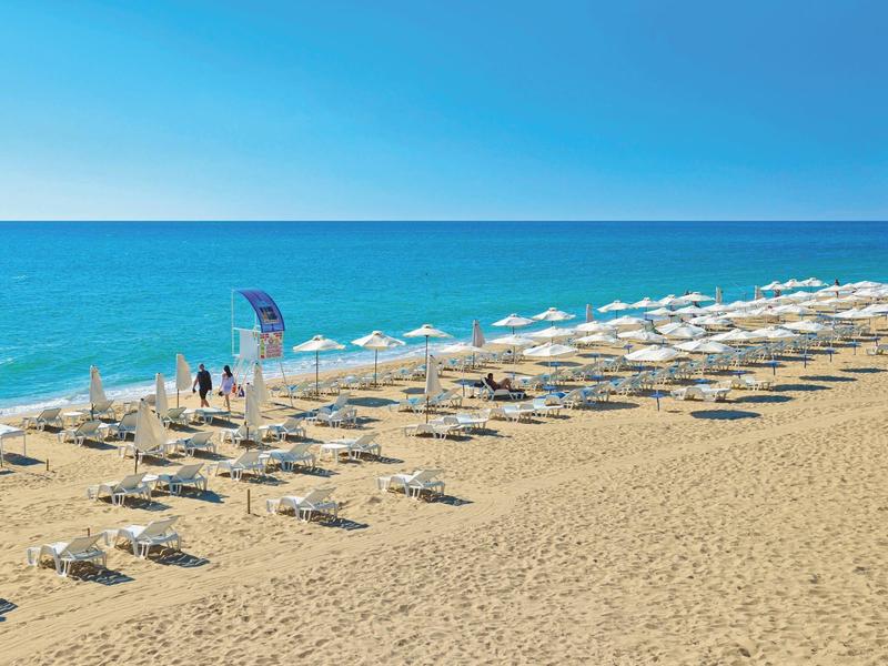 Strand mit Sonnenliegen und weißen Sonnenschirmen am Meer unter klarem Himmel.