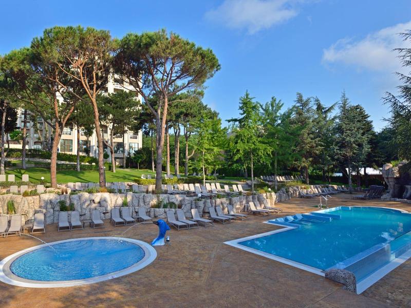 Poolbereich mit Kinderpool und großem Schwimmbecken umgeben von Liegestühlen und Bäumen.