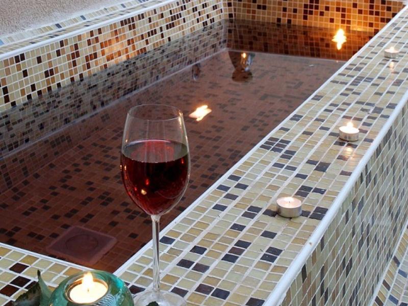 Ein rechteckiges Mosaikbad mit rotem Wasser, Kerze und Glas Rotwein auf der Kante.