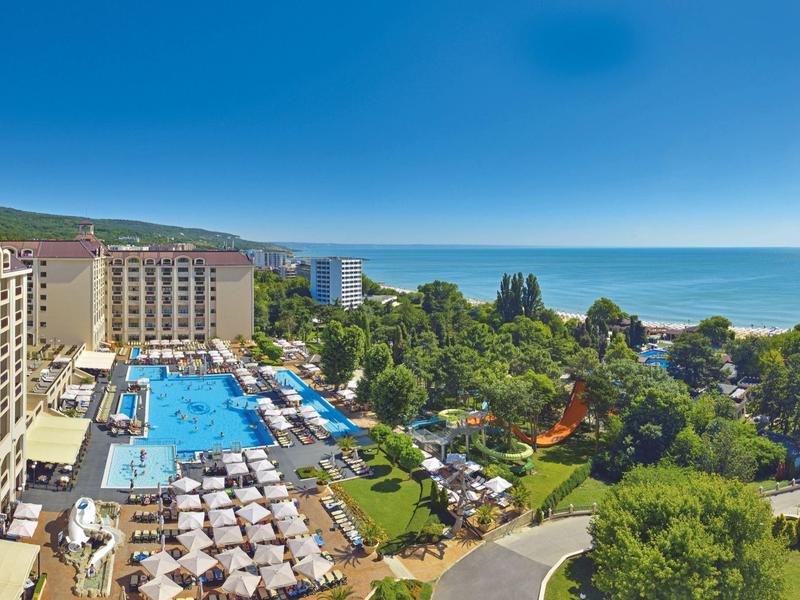 Hotelresort mit großen Außenpools, Sitzbereichen, viel Grün und Blick auf das Meer.