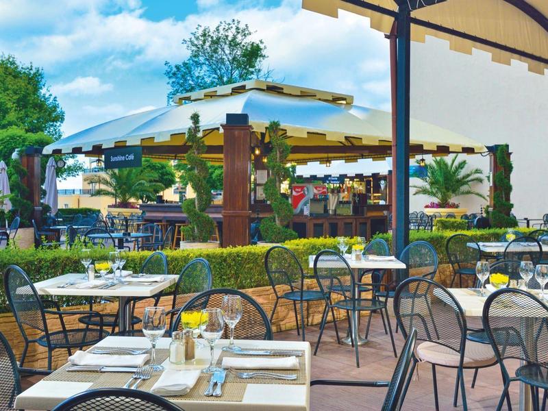 Terrasse eines Cafés mit gedeckten Tischen und Stühlen unter einem Sonnendach.