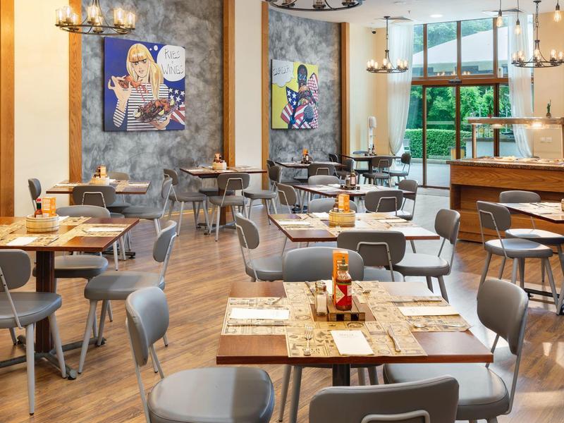 Modernes Restaurant mit Holzboden, grauen Stühlen und lebhaften Kunstwerken an den Wänden.