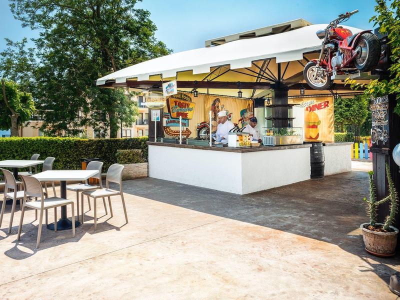 Moderner Außenbarbereich mit Stühlen, Tischen und einem schattigen Sonnenschirm, Motorrad-Dekoration oben.