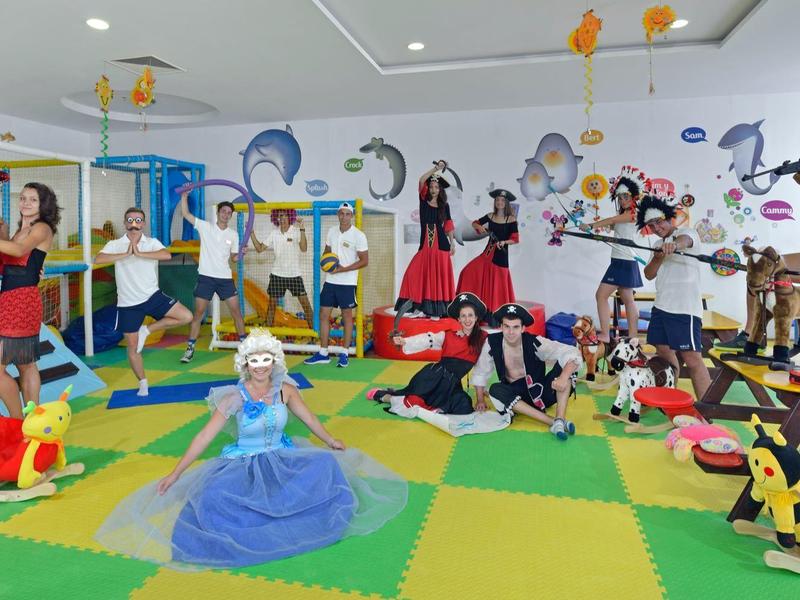 Kinder und Erwachsene in farbenfrohen Kostümen spielen und posieren in einem hellen Raum mit Spielmatten.