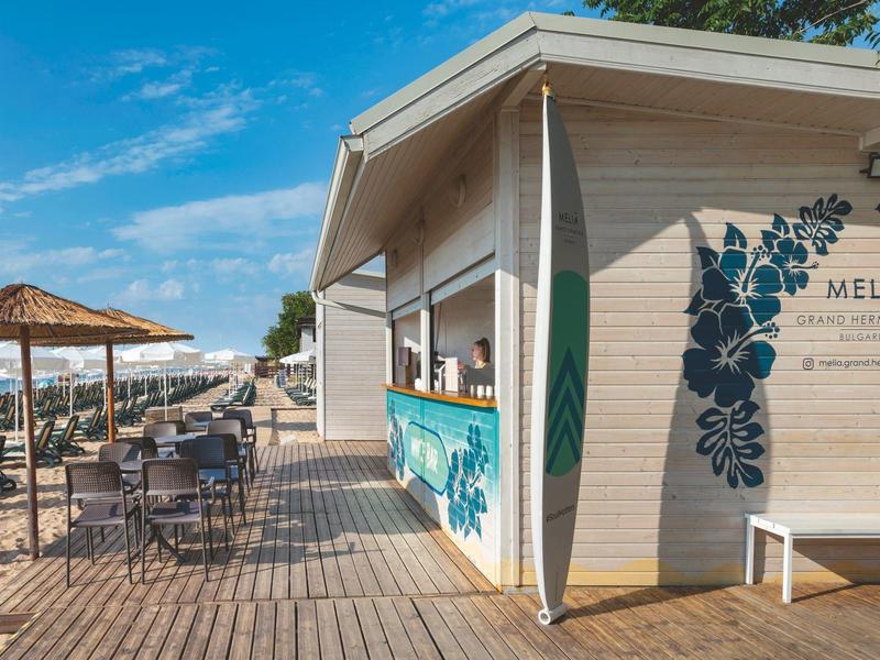 Strandbar mit Holzboden, Sitzgelegenheiten und Sonnenschirmen bei klarem Himmel