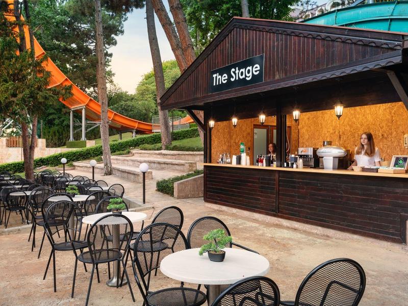 Holzbar namens The Sloge mit Tischen und Stühlen im Freien unter Bäumen.