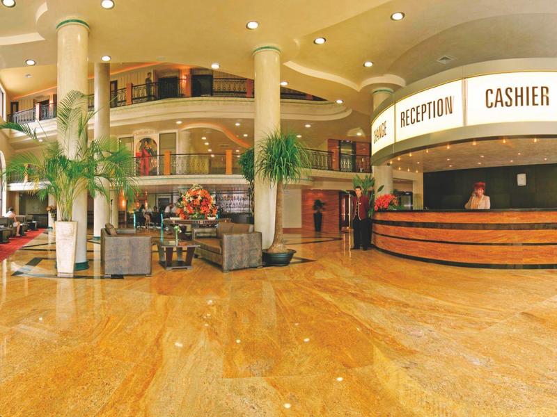 Große Hotellobby mit glänzendem Marmorboden, Empfangstresen, Palmen und hoher Decke.