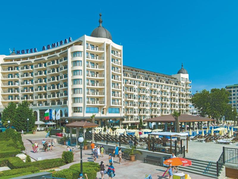 Großes Hotelgebäude mit weißer Fassade, mehreren Balkonen und grünen Gärten im Vordergrund.