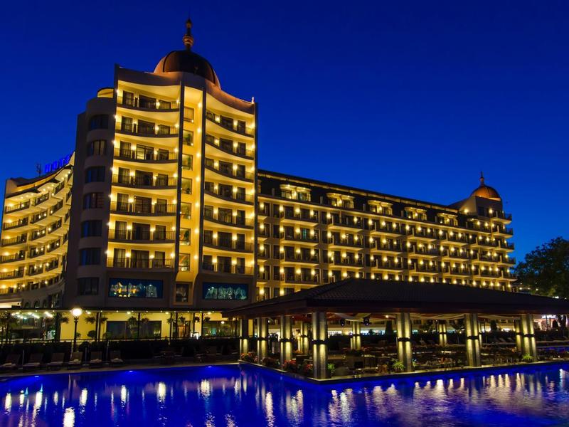 Großes Hotel bei Nacht, viele gelb beleuchtete Fenster und blau beleuchteter Pool im Vordergrund.