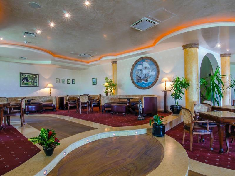 Eleganter Gastraum mit roten Teppichen, runden Tischen, Pflanzen und dekorativer Deckenbeleuchtung.