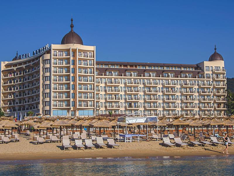 Großes Hotelgebäude am Strand mit vielen Liegestühlen und Sonnenschirmen unter klarem Himmel.